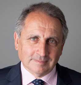 Headshot of a middle-aged man with grey hair, wearing a dark suit and dark patterned tie.