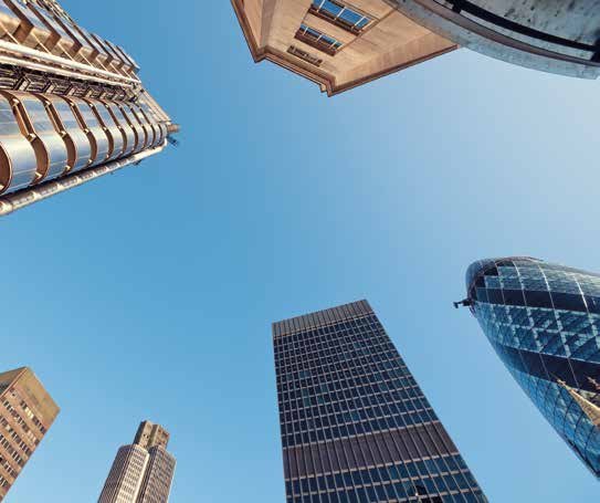 Low-angle view of multiple modern skyscrapers and office buildings reaching into a clear blue sky.