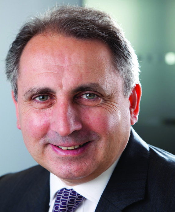 Professional headshot of a middle-aged man with short dark and grey hair, wearing a suit and patterned tie.