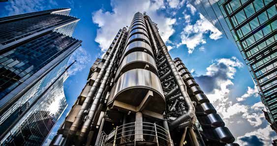 Low-angle view of the iconic Lloyd's building in London, surrounded by other modern skyscrapers, under a blue sky.