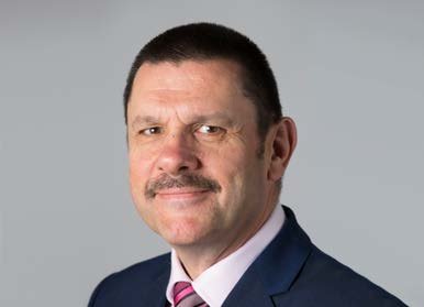 Headshot of a man with a mustache, wearing a dark suit and pink and blue striped tie.