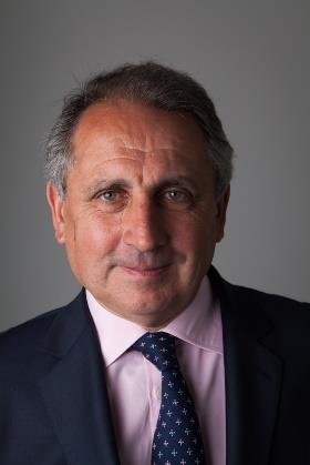 Headshot of a smiling man with graying hair, wearing a navy suit, pink shirt, and patterned blue tie.