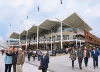 Exterior view of a modern building with a multi-peaked roof, featuring multiple levels and people walking in front.