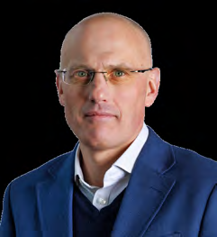 Headshot of a bald man with glasses, wearing a blue blazer and sweater, looking directly at the camera.