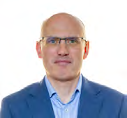 Headshot of a bald man with glasses, wearing a light blue shirt and dark blazer.