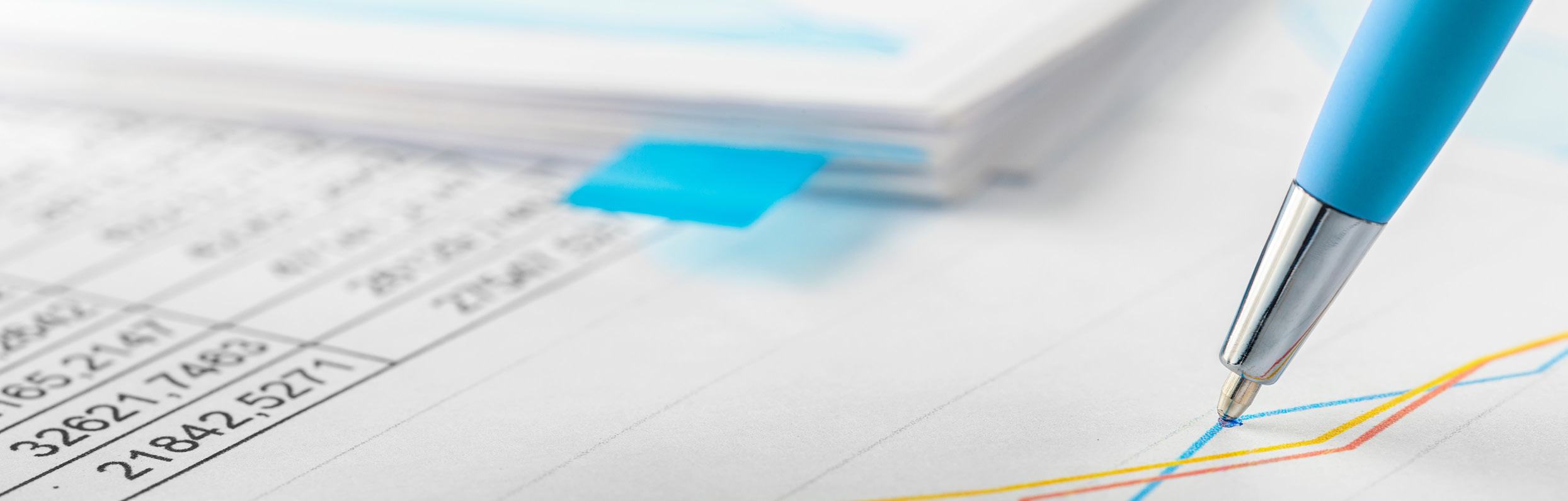 Close-up of a pen on a document showing a line graph and blurred numerical data, suggesting financial analysis or reporting.