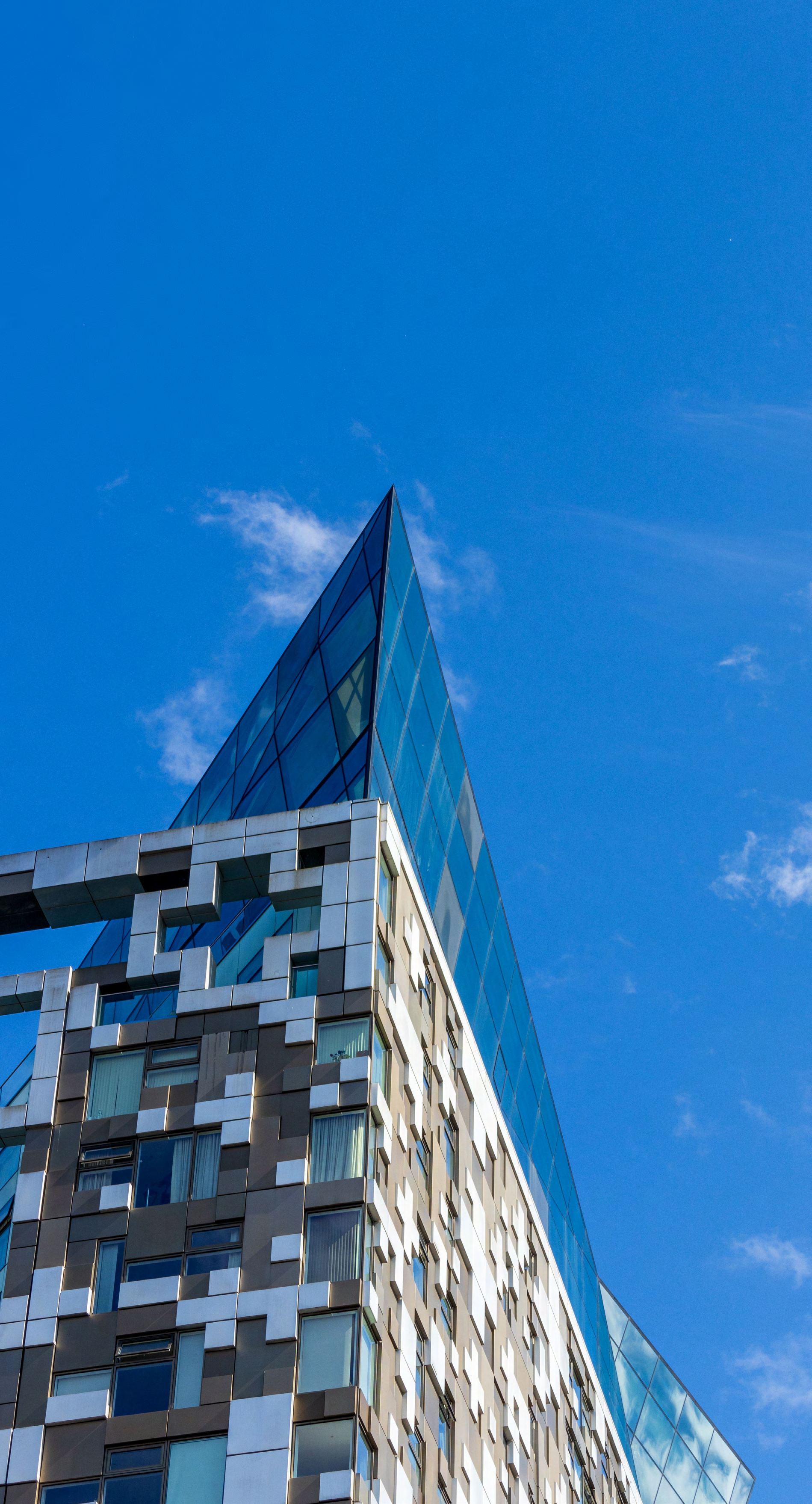 Low-angle view of a modern glass and steel building with a sharp, geometric design and a triangular glass peak, set against a clear blue sky.