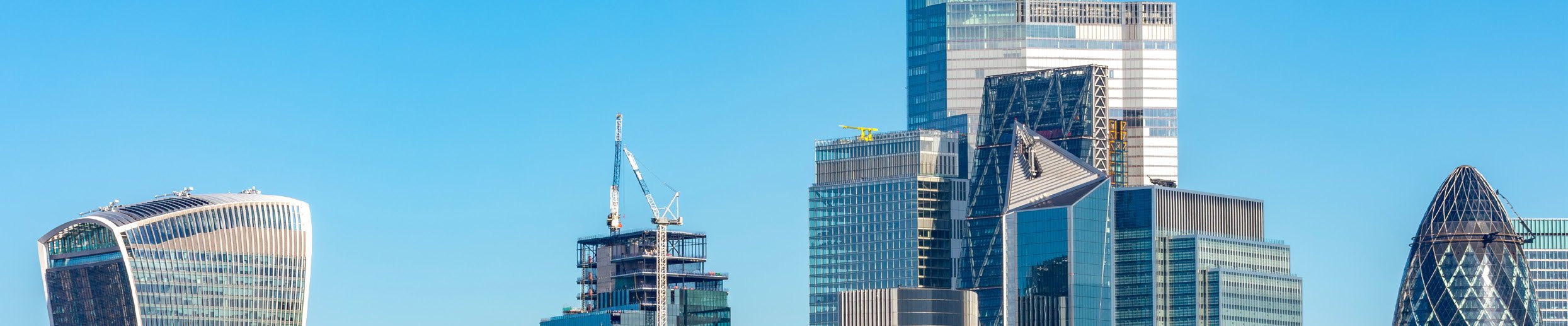 Skyline of modern skyscrapers in London, including 20 Fenchurch Street and 30 St Mary Axe, with a building under construction, against a clear blue sky.