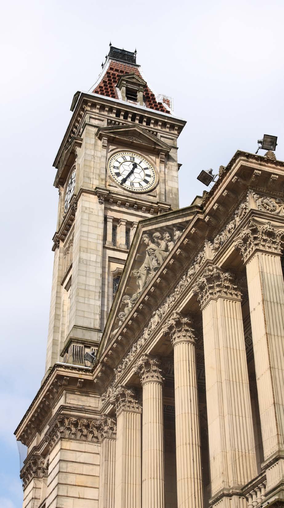 Historical stone building featuring a large clock tower with Roman numerals and classical columns at its base.