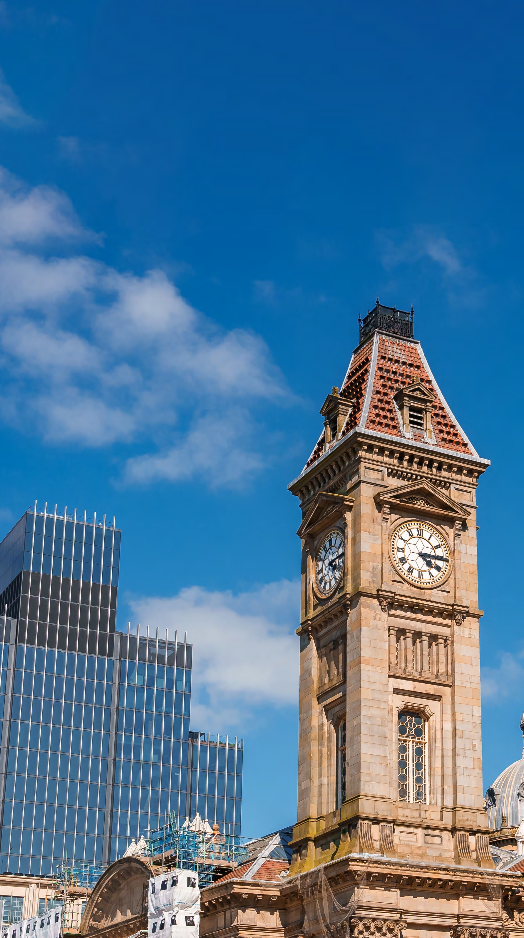 Historical clock tower and modern glass skyscraper under a blue sky, illustrating urban architectural contrast.