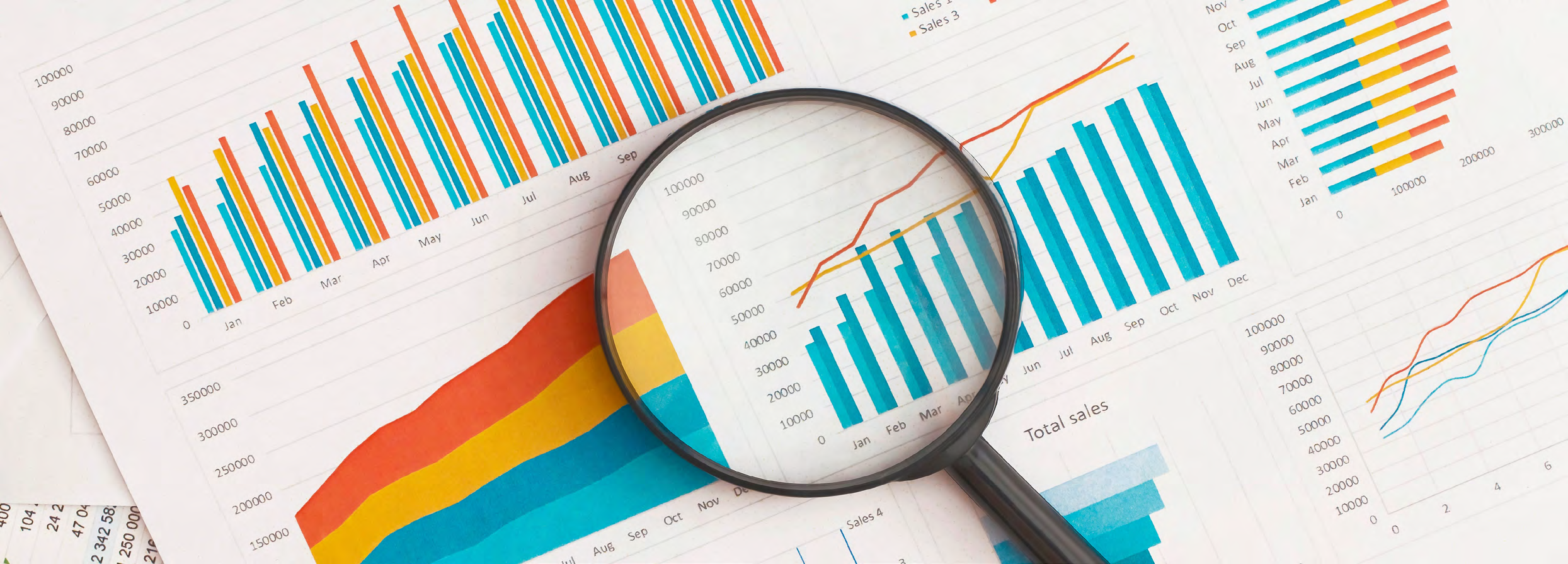Overhead view of several financial charts and graphs, including bar charts and line graphs, with a magnifying glass placed over one chart, symbolizing data analysis.