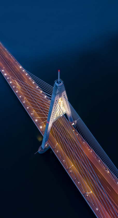 Aerial view of a modern cable-stayed bridge lit up at night over dark water.