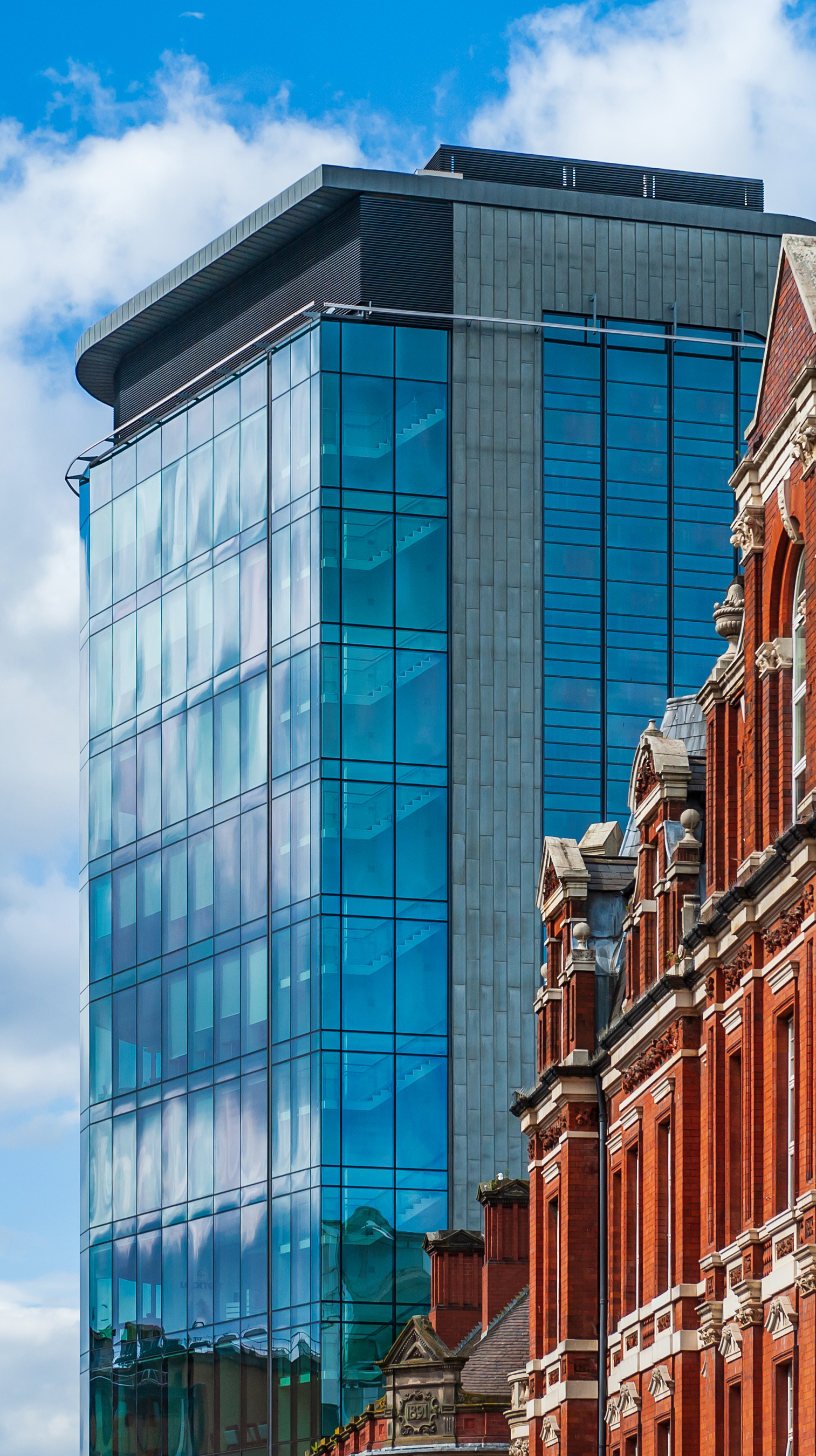 Modern glass skyscraper stands beside an ornate, historic red brick building, highlighting architectural contrast.