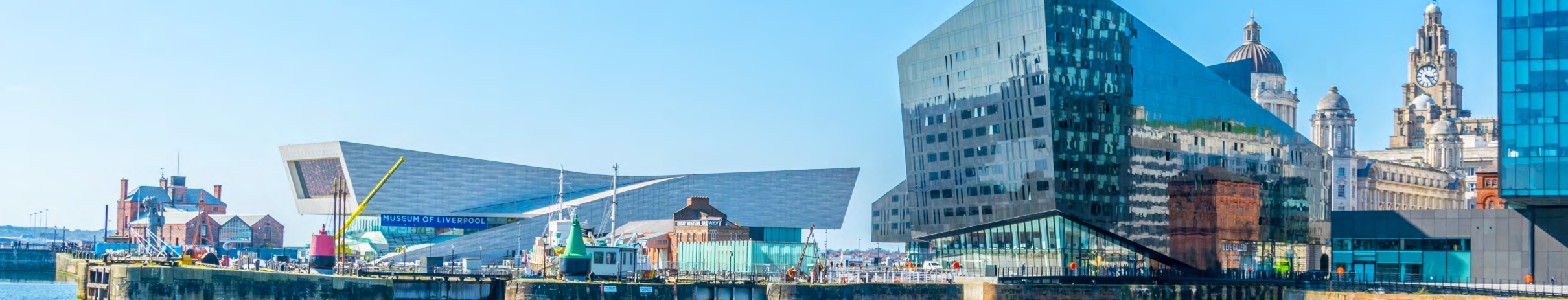 Panoramic view of Liverpool waterfront featuring the Museum of Liverpool, modern glass buildings, and the historic Royal Liver Building under a clear blue sky.
