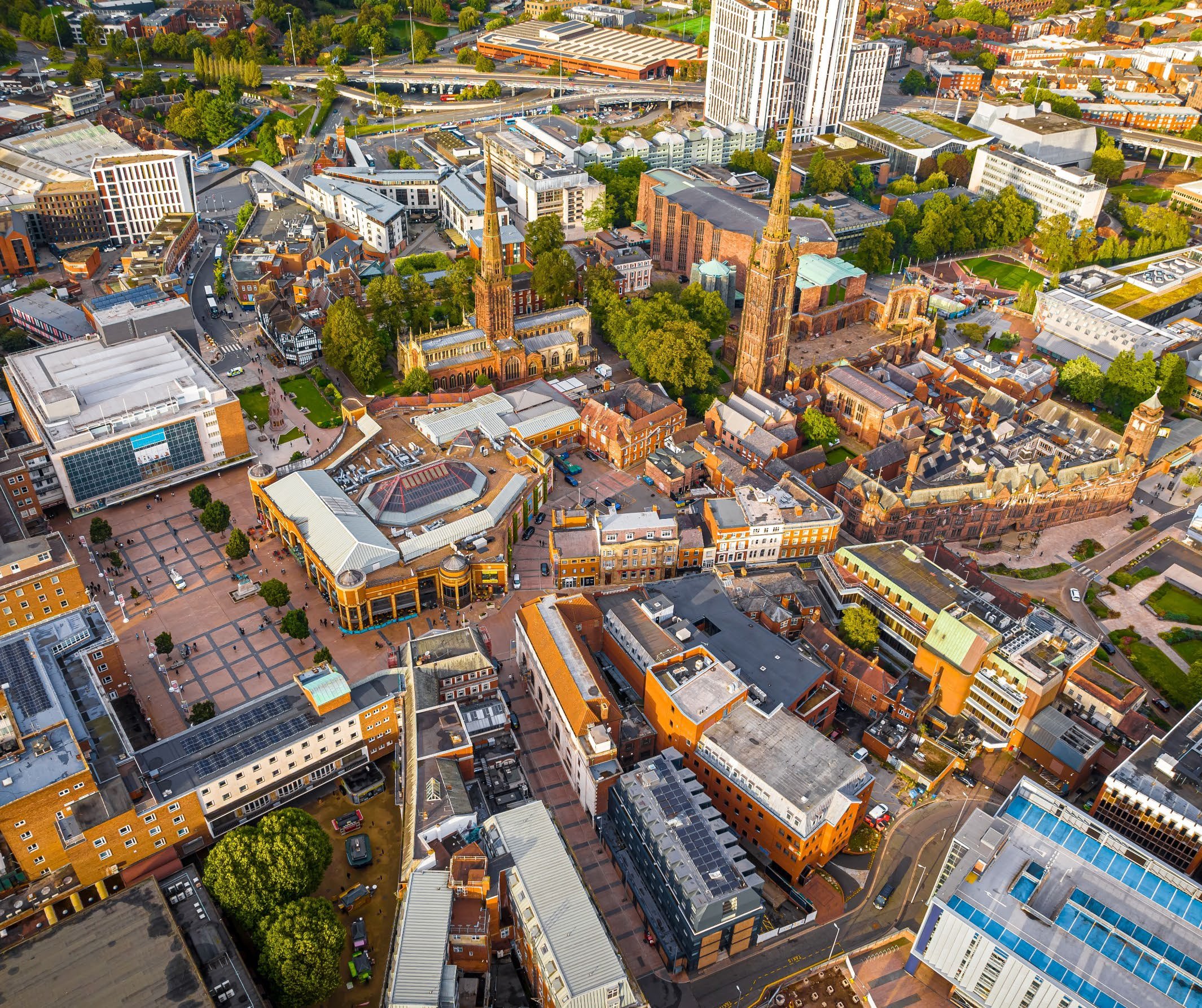 Aerial view of a city showing diverse architecture, roads, and green spaces, with prominent church spires dominating the skyline.