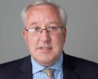 Headshot of a middle-aged man with glasses and grey hair, wearing a dark pinstripe suit and patterned tie.
