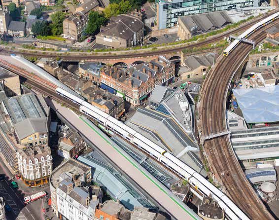 Aerial view of multiple intertwined railway lines with a train on tracks, surrounded by urban buildings and infrastructure.