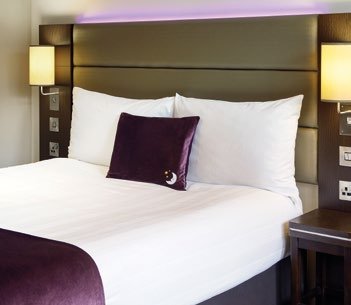 A neatly made hotel bed with white duvet, a purple throw, and a purple decorative pillow.