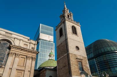 Historical church tower and green dome juxtaposed with modern glass skyscrapers under a blue sky.