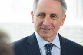 Portrait of a smiling older man with grey hair, wearing a dark suit and a patterned blue tie.
