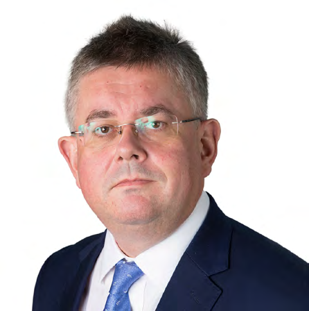 Headshot of a middle-aged man with glasses, wearing a blue suit and tie, against a white background.
