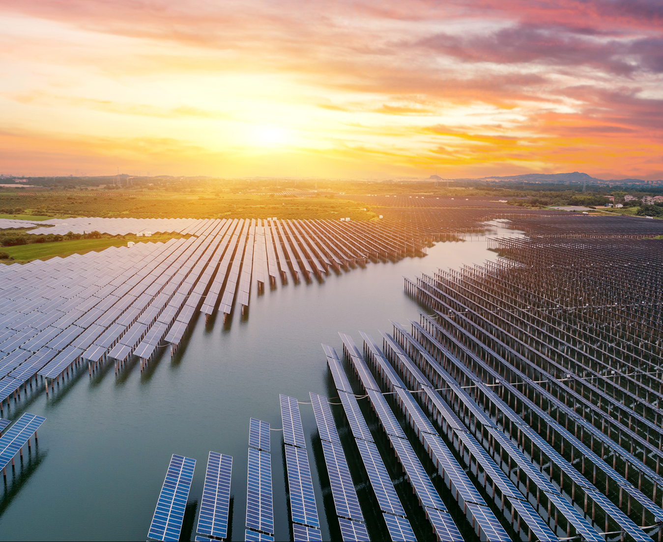 Aerial view of a large solar farm with panels arranged over water, under a vibrant sunset sky.