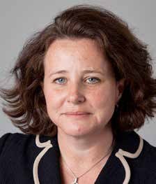 Headshot of a woman with brown, curly hair and blue eyes, wearing a dark top and necklace.