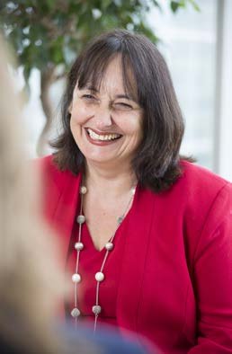 Portrait of a smiling woman with dark hair, wearing a red jacket and a multi-strand necklace.