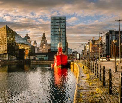 Liverpool cityscape featuring modern buildings, historic architecture, and a prominent red ship docked in the foreground.