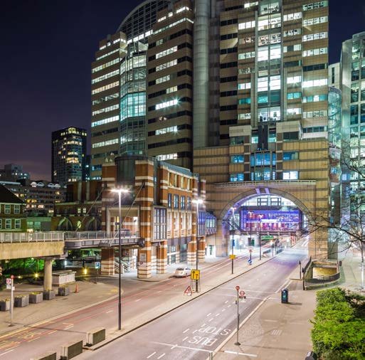 Night view of a modern city street lined with illuminated high-rise buildings and an overhead archway structure.