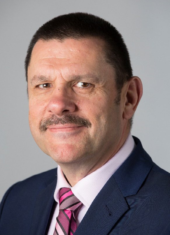 Headshot of a man with a mustache, wearing a dark blue suit and a pink striped tie.