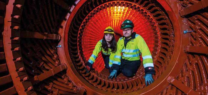 Two workers in safety gear inside a large industrial machine, likely a generator or turbine casing.