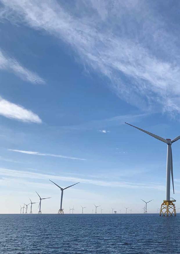 Offshore wind farm with numerous turbines visible in the ocean under a blue sky.