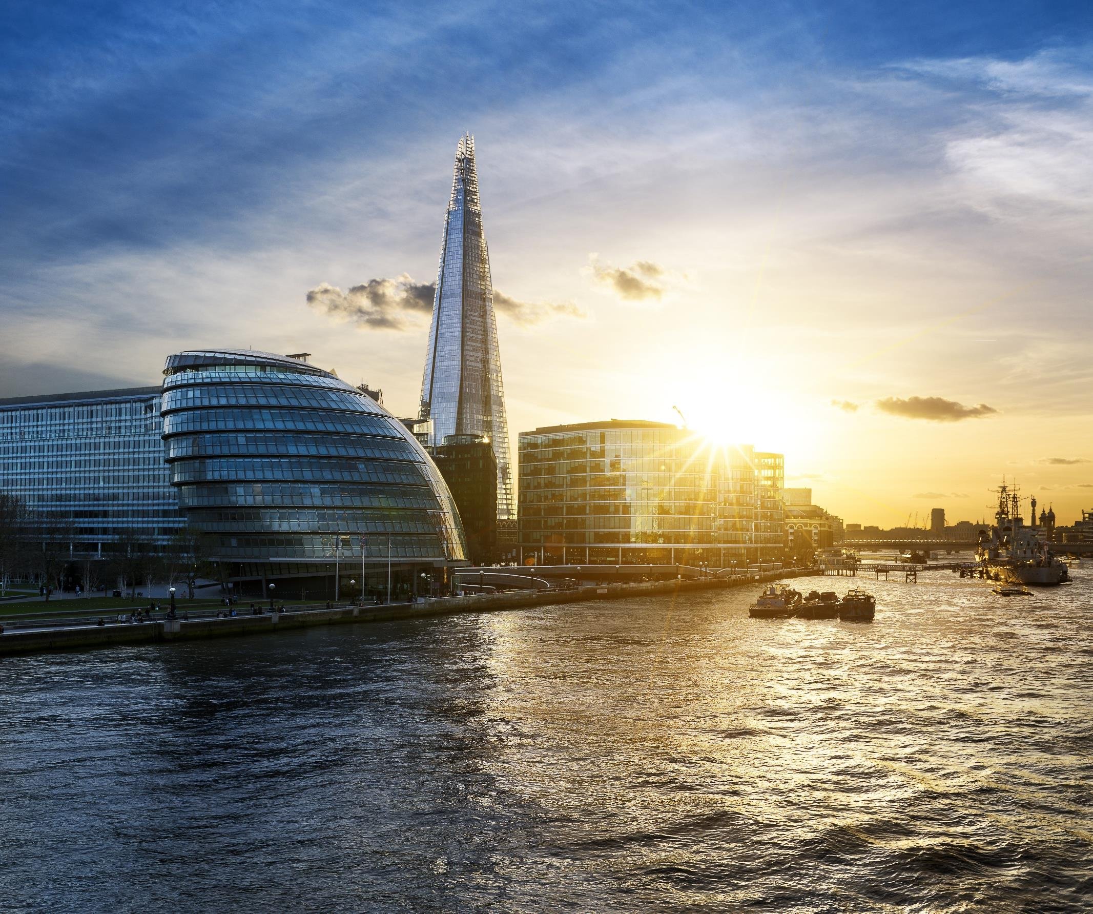 Sunset view of the River Thames with London's City Hall, The Shard skyscraper, and HMS Belfast in the background.