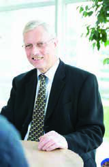 A man in a suit and tie, wearing glasses, smiling during a meeting.