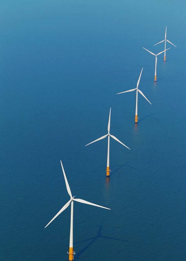 Aerial view of several offshore wind turbines in a line over blue water.