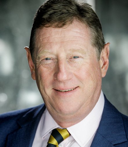 Headshot of a smiling man with light brown hair, wearing a dark blue suit, light shirt, and striped yellow and blue tie.