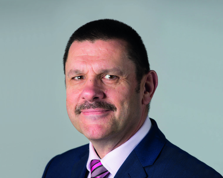 Headshot of a man with short dark hair, a mustache, wearing a dark suit and pink striped tie.
