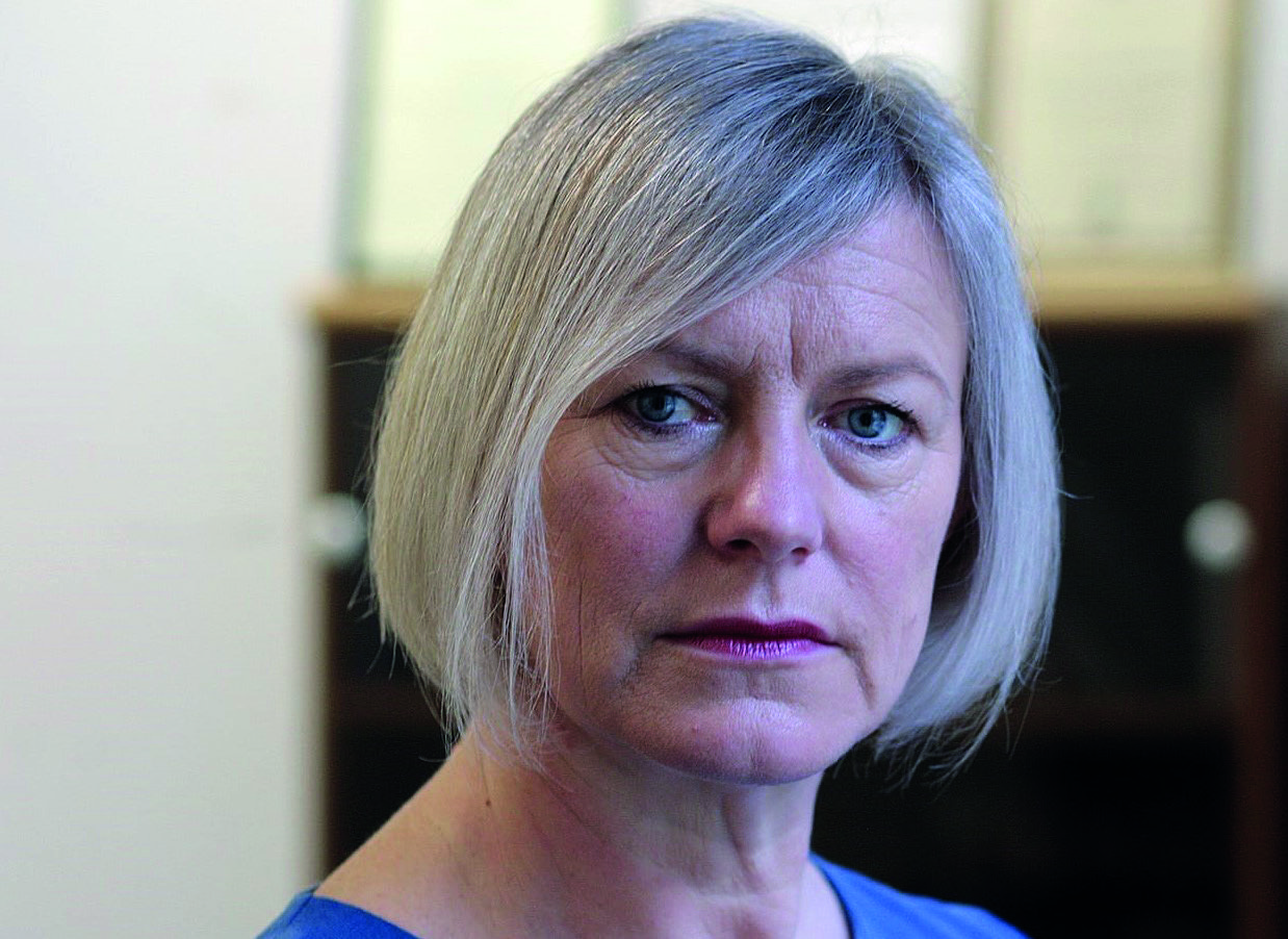 Portrait of a woman with short grey hair and blue eyes, looking seriously at the camera.