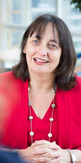 Portrait of a smiling woman with dark hair, wearing a red jacket and a long beaded necklace.
