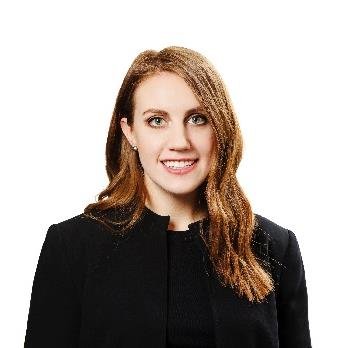 Professional headshot of a smiling woman with long brown hair wearing a black blazer.