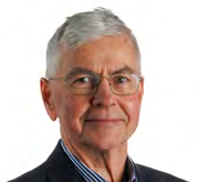 Headshot of a smiling older man with grey hair and glasses, wearing a dark suit.