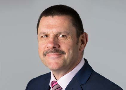 Headshot of a man with short dark hair and a mustache, wearing a dark suit and a pink striped tie.