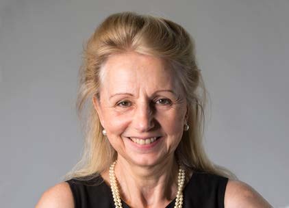 Headshot of a woman with blonde hair, wearing a black top and pearl necklace, smiling slightly.