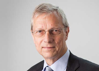 Portrait of an older man with grey hair and glasses, wearing a suit and tie.