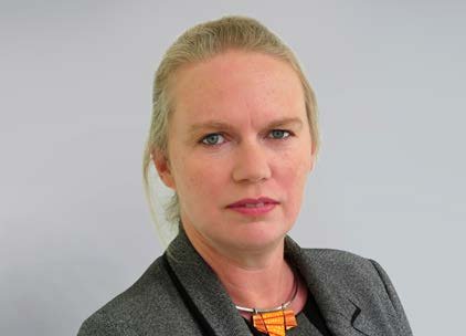 Portrait of a woman with blonde hair pulled back, wearing a grey jacket and orange necklace.