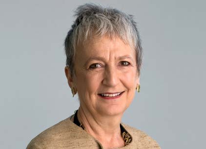 Portrait of an older woman with short grey hair, smiling, wearing a beige top and gold earrings.