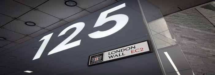 Low-angle view of a modern office building with number 125 on its facade, under a blue sky with a plane.