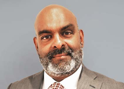 Portrait of a man with a bald head and a grey beard, wearing a suit and patterned tie.