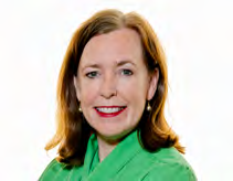 Headshot of a woman with red hair and a green top, smiling broadly.